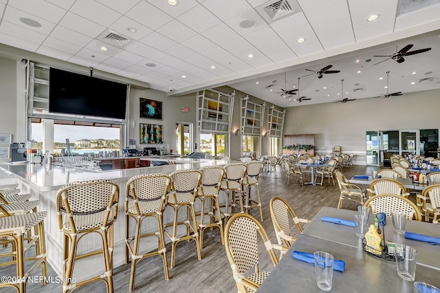 dining room with a towering ceiling, a wealth of natural light, a drop ceiling, and light wood-type flooring