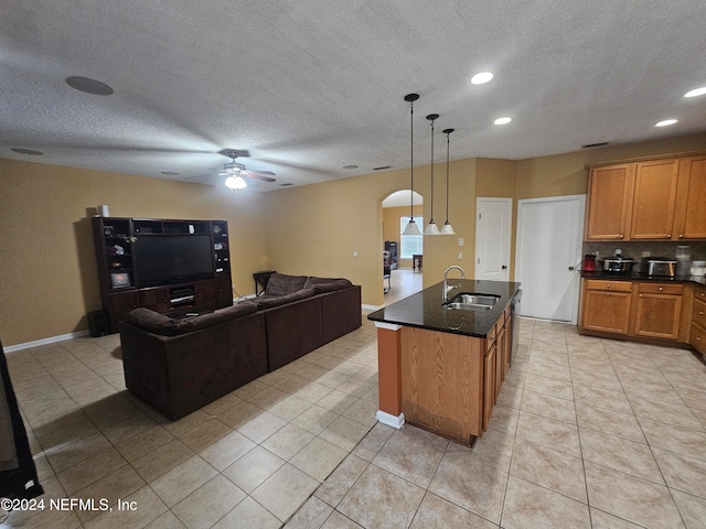 kitchen with light tile patterned flooring, ceiling fan, pendant lighting, sink, and a kitchen island with sink