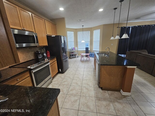 kitchen with appliances with stainless steel finishes, sink, hanging light fixtures, decorative backsplash, and a kitchen island with sink