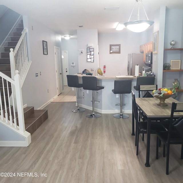 dining space featuring light wood finished floors, stairway, visible vents, and baseboards