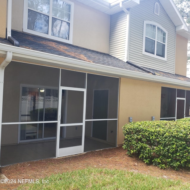 rear view of property with a sunroom, roof with shingles, and stucco siding