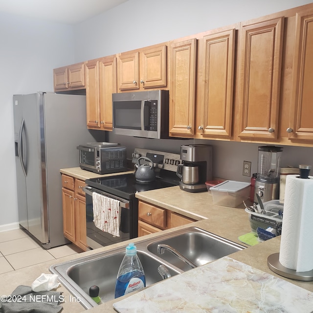 kitchen with a toaster, light tile patterned floors, light countertops, appliances with stainless steel finishes, and a sink