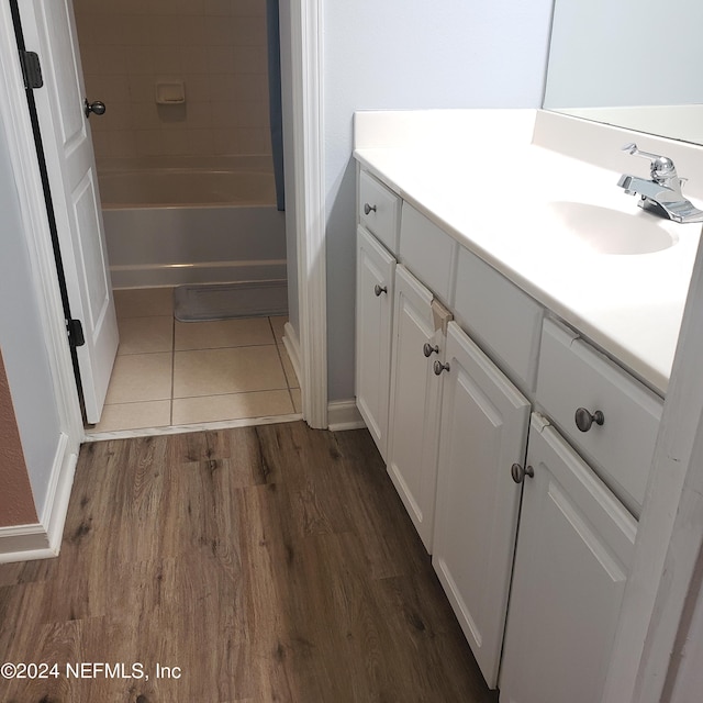 full bath with washtub / shower combination, vanity, and wood finished floors