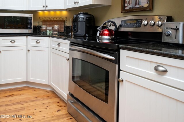 kitchen with light wood-type flooring, stainless steel appliances, dark stone counters, and white cabinetry