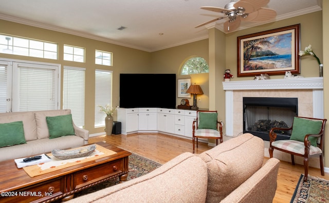 living room with a tiled fireplace, light wood-type flooring, ornamental molding, and ceiling fan