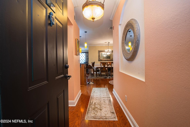 hall featuring baseboards, dark wood-style flooring, and an inviting chandelier