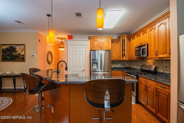 kitchen with wood-type flooring, hanging light fixtures, decorative backsplash, an island with sink, and appliances with stainless steel finishes