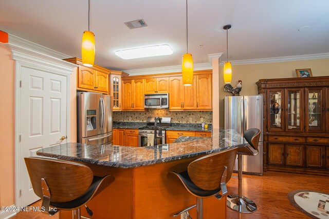 kitchen featuring a breakfast bar, backsplash, a kitchen island with sink, appliances with stainless steel finishes, and hardwood / wood-style flooring