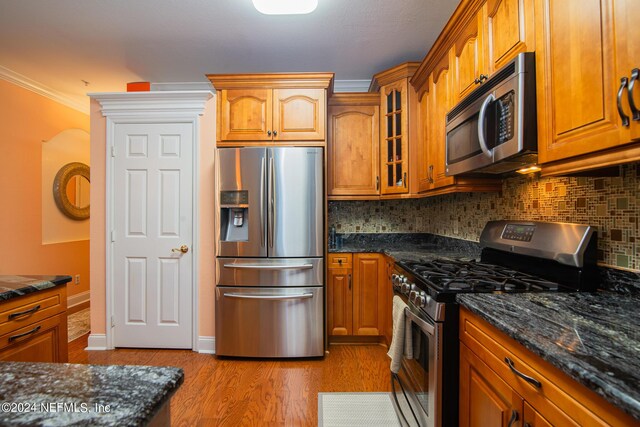 kitchen with crown molding, dark stone counters, backsplash, light hardwood / wood-style floors, and appliances with stainless steel finishes