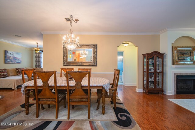 dining space with hardwood / wood-style flooring, ceiling fan with notable chandelier, a fireplace, and ornamental molding