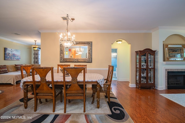 dining room featuring arched walkways, a tiled fireplace, wood finished floors, and crown molding