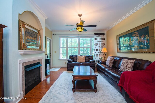 living room with crown molding, hardwood / wood-style flooring, a tile fireplace, and ceiling fan