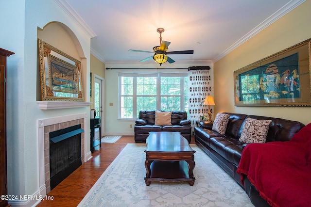 living area with baseboards, a tile fireplace, ceiling fan, ornamental molding, and wood finished floors