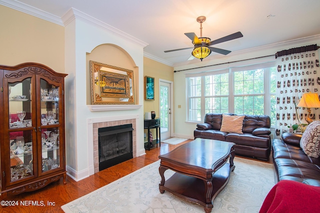 living room with ceiling fan, wood finished floors, baseboards, a tiled fireplace, and crown molding