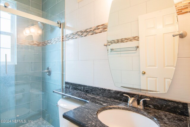 bathroom with tile walls, a shower with door, toilet, and vanity