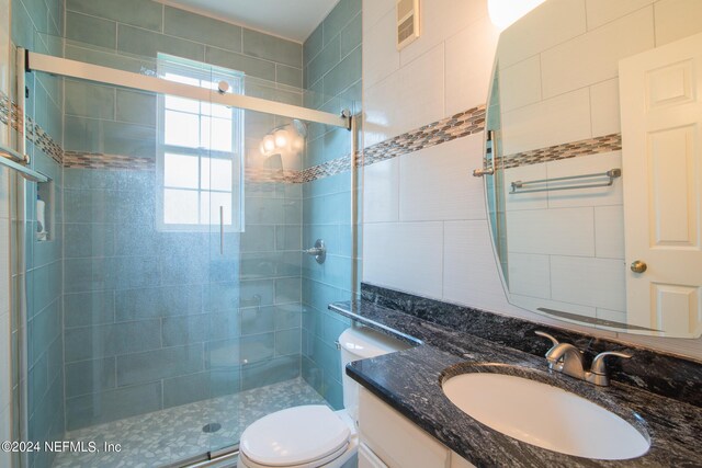 bathroom featuring tile walls, a shower with door, toilet, and vanity