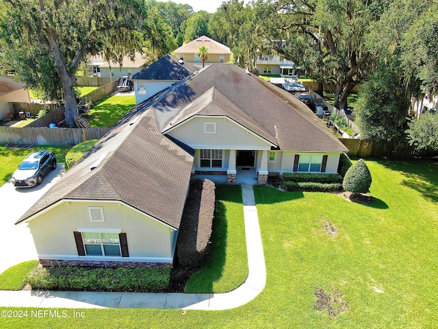 view of front facade with a shingled roof, fence, stone siding, stucco siding, and a front yard