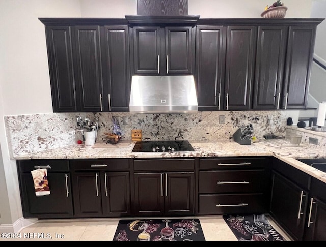 kitchen featuring black electric cooktop, under cabinet range hood, dark cabinetry, decorative backsplash, and light stone countertops