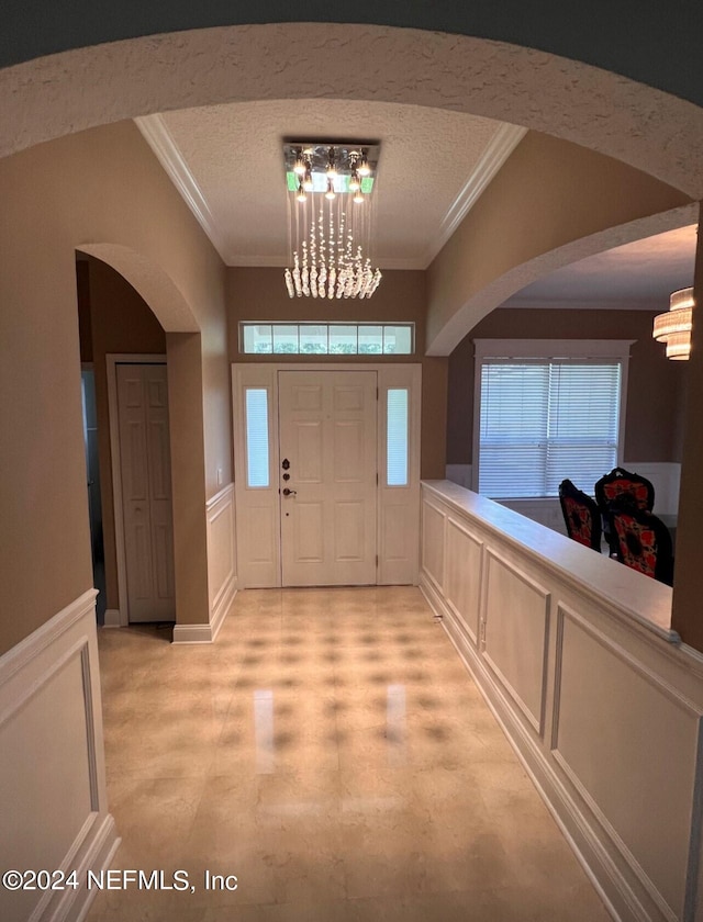 foyer with crown molding, a chandelier, and a decorative wall