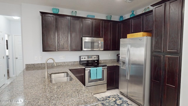 kitchen with light stone countertops, light tile patterned flooring, appliances with stainless steel finishes, sink, and dark brown cabinets