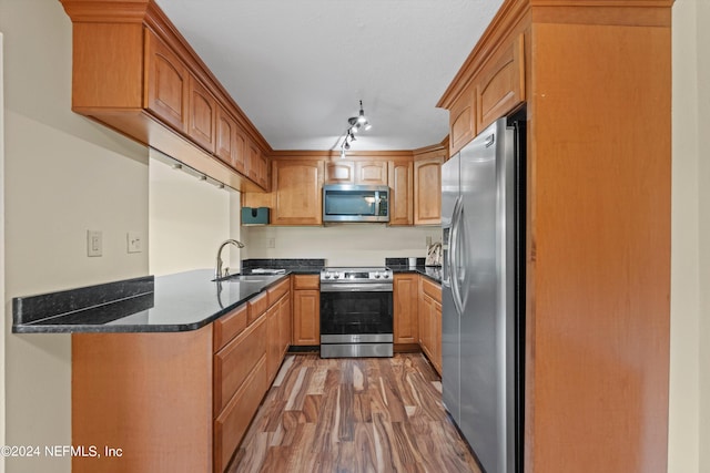 kitchen featuring appliances with stainless steel finishes, dark stone counters, sink, kitchen peninsula, and wood-type flooring