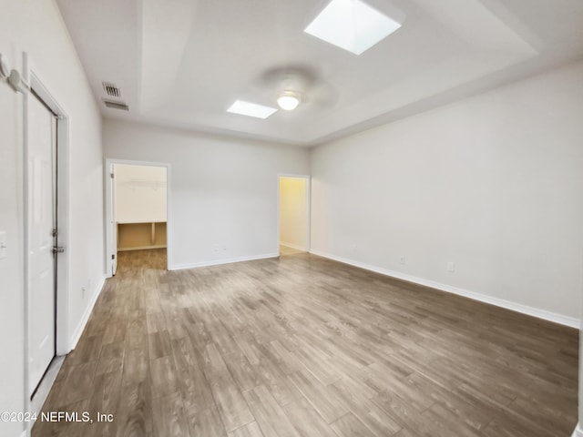 unfurnished bedroom with hardwood / wood-style floors, a skylight, a walk in closet, ceiling fan, and a closet