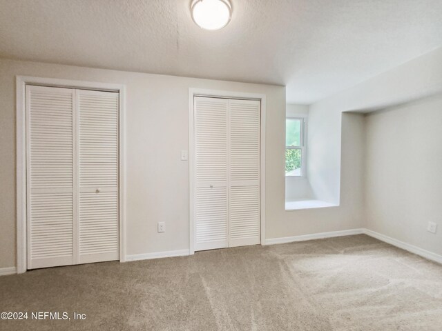 unfurnished bedroom featuring a textured ceiling, multiple closets, and carpet flooring