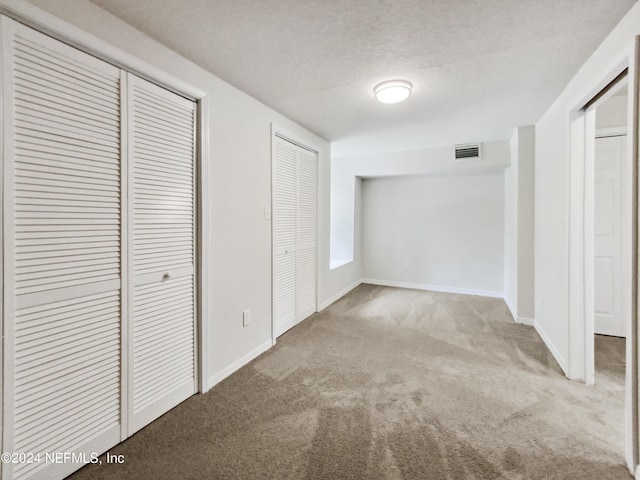 interior space featuring light carpet, a textured ceiling, and multiple closets