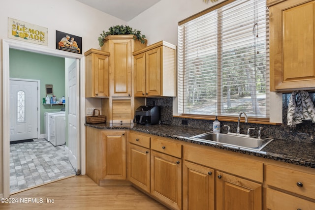 kitchen with sink, dark stone countertops, light hardwood / wood-style flooring, washing machine and clothes dryer, and tasteful backsplash