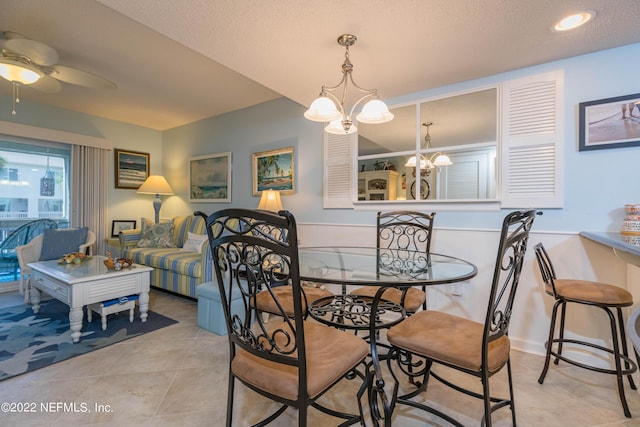 dining space with light tile patterned floors, ceiling fan with notable chandelier, and a textured ceiling