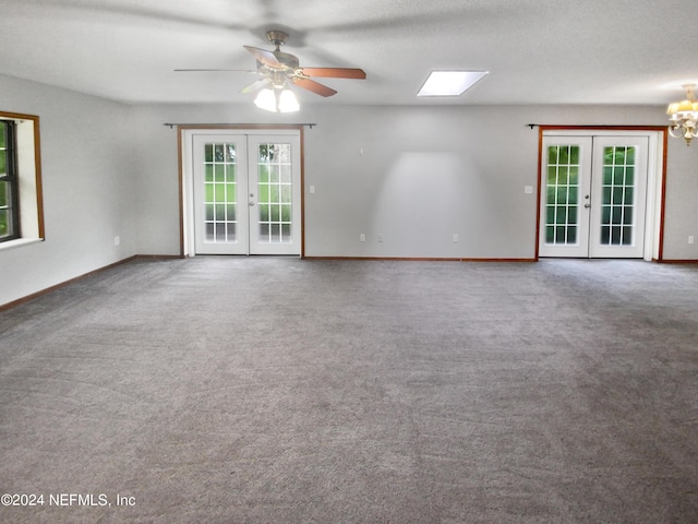 carpeted empty room featuring ceiling fan with notable chandelier, a skylight, french doors, and a textured ceiling