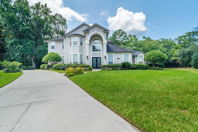 view of front of property with stucco siding, a front lawn, concrete driveway, and french doors