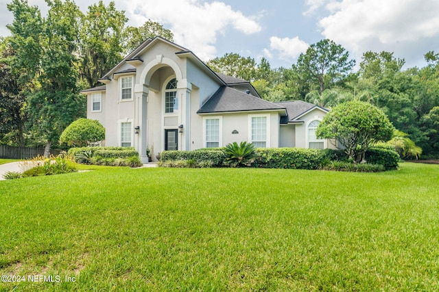 view of front of property featuring roof with shingles, a front lawn, and stucco siding