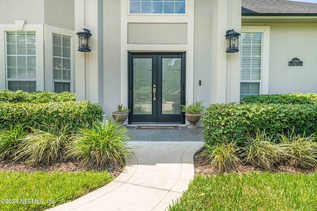 property entrance with stucco siding, a shingled roof, and french doors