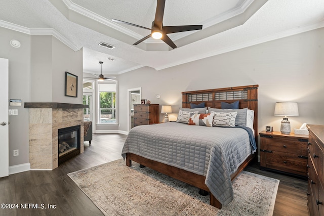 bedroom with dark wood-style floors, a fireplace, ornamental molding, and a raised ceiling