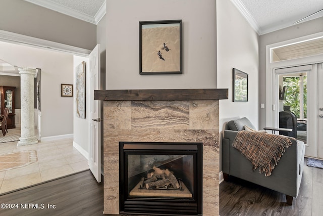 living room with ornamental molding, a glass covered fireplace, a textured ceiling, wood finished floors, and ornate columns