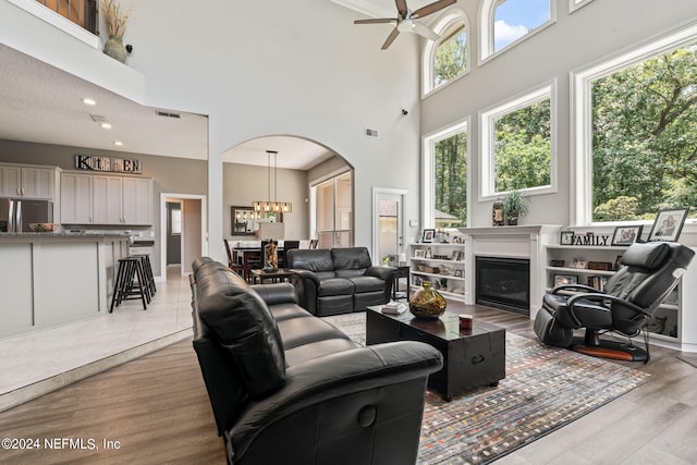 living area featuring visible vents, a towering ceiling, a glass covered fireplace, and light wood-style flooring