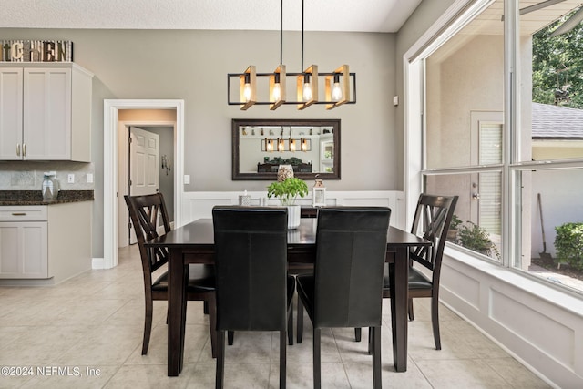 dining room with a wainscoted wall, light tile patterned floors, a decorative wall, and an inviting chandelier