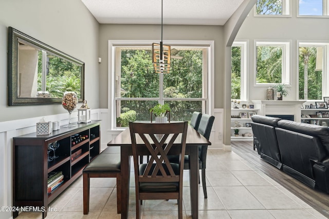 dining room featuring light tile patterned floors, wainscoting, a textured ceiling, a fireplace, and a decorative wall