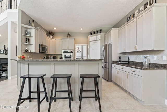 kitchen with a breakfast bar area, open shelves, decorative backsplash, appliances with stainless steel finishes, and dark stone countertops