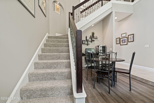 stairs featuring a towering ceiling, baseboards, and wood finished floors