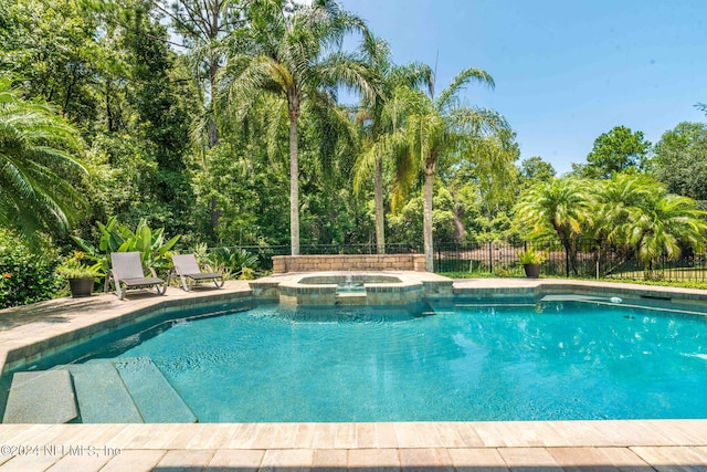 view of pool with fence and a pool with connected hot tub