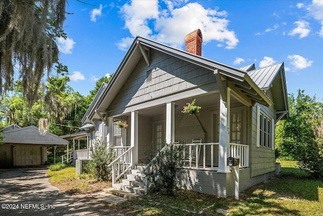 view of front of house featuring a garage, a chimney, metal roof, a standing seam roof, and a porch