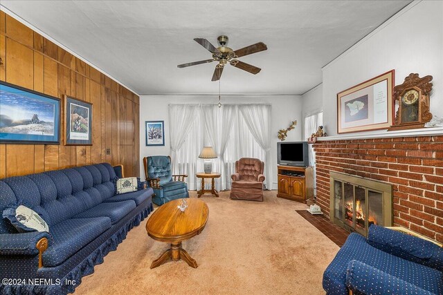 living room featuring wooden walls, ceiling fan, a brick fireplace, and carpet flooring