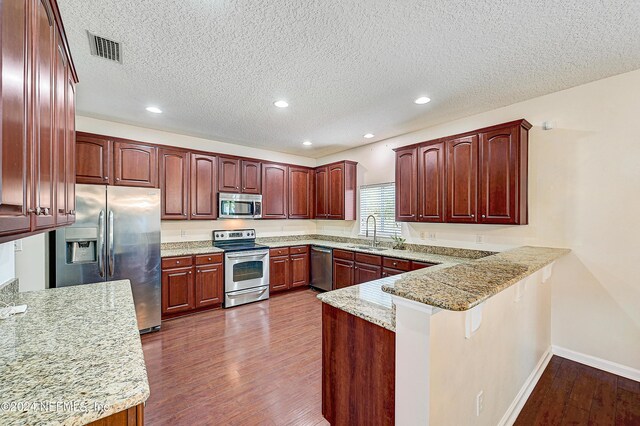 kitchen featuring a textured ceiling, light stone counters, kitchen peninsula, stainless steel appliances, and dark hardwood / wood-style flooring