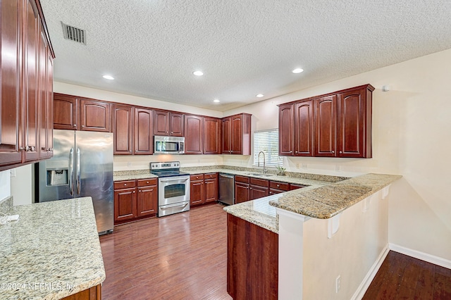 kitchen with visible vents, dark wood-style floors, appliances with stainless steel finishes, a peninsula, and a sink