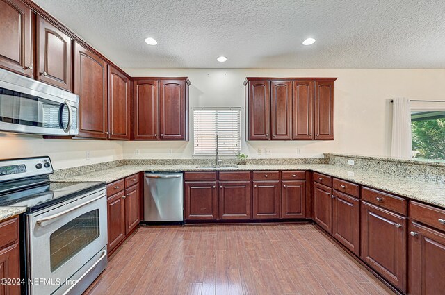 kitchen with stainless steel appliances, a textured ceiling, hardwood / wood-style floors, sink, and light stone counters