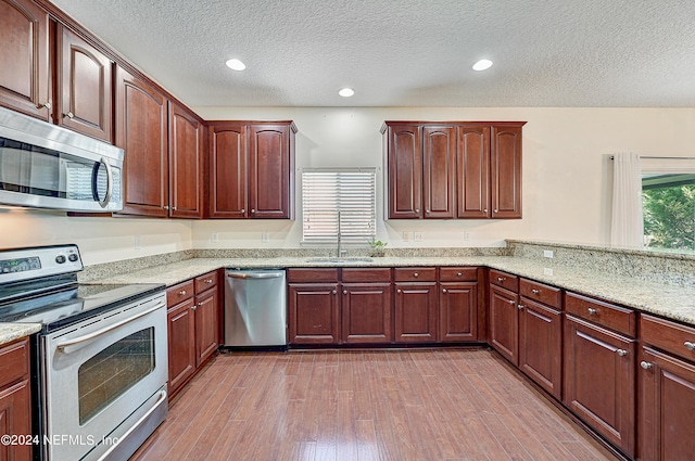 kitchen featuring light stone counters, recessed lighting, stainless steel appliances, a sink, and light wood-style floors