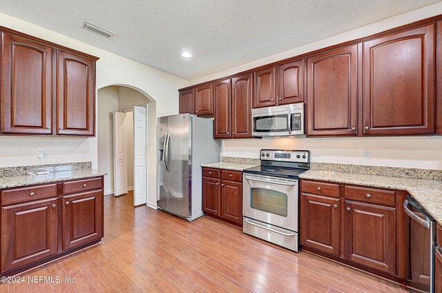 kitchen with a textured ceiling, light stone countertops, stainless steel appliances, and light hardwood / wood-style floors