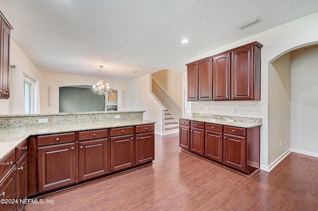 kitchen featuring light stone counters, decorative light fixtures, visible vents, wood finished floors, and a peninsula